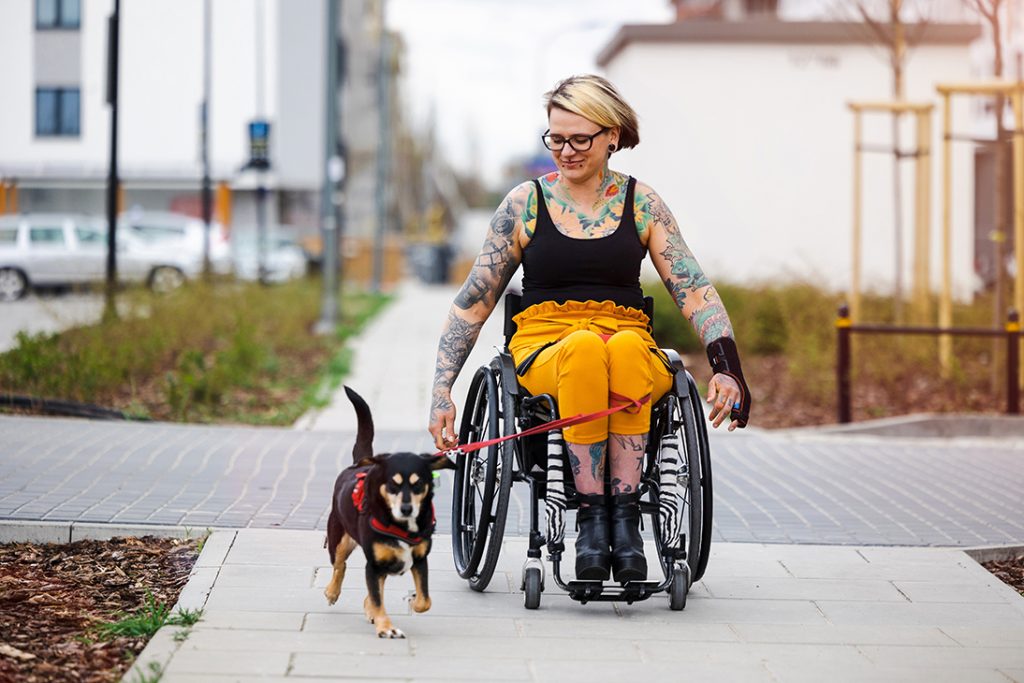 Junge Frau mit Tattoos im Rollstuhl geht mit ihrem Hund gassi. SAB NRW Bochum Startseite